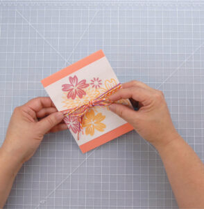 person tying yarn around a card with pink and orange flowers on the front